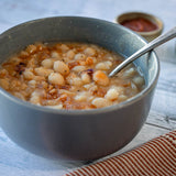 A bowl of white Caballero beans from Rancho Gordo with a spoon in it, near a red-striped napkin