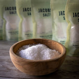 A bowl of Jacobsen Pure Flake Sea Salt with six bags in the background 