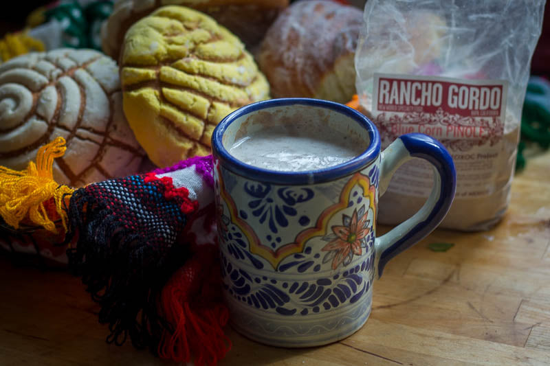 A mug with atole with the Pinole Azul bag in the background and Mexican Pastries