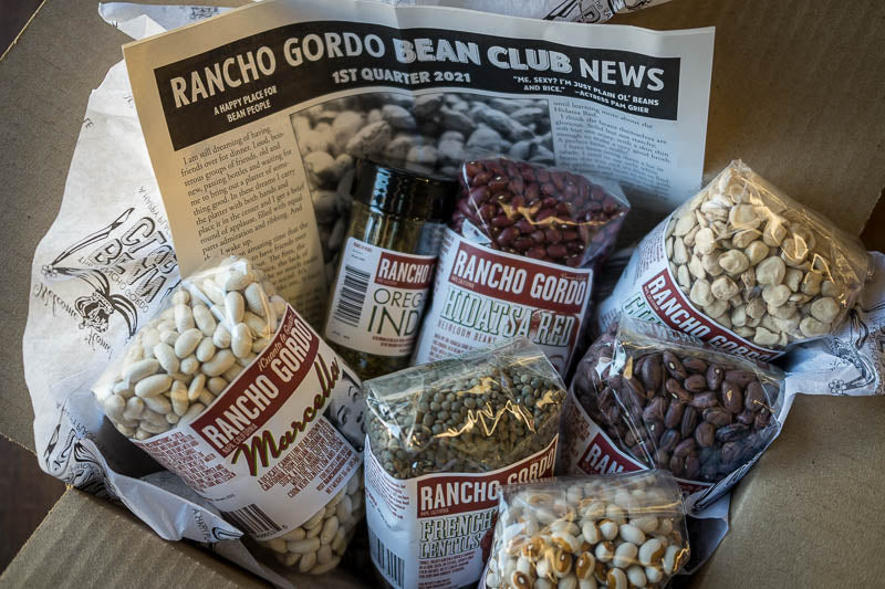 An Open box of the Bean Club with Marcella, Hidatsa Red, Cicerchia, French green lentils, Yellow Eye, Rio Zape, a jar of Oregano Indio, and recipes