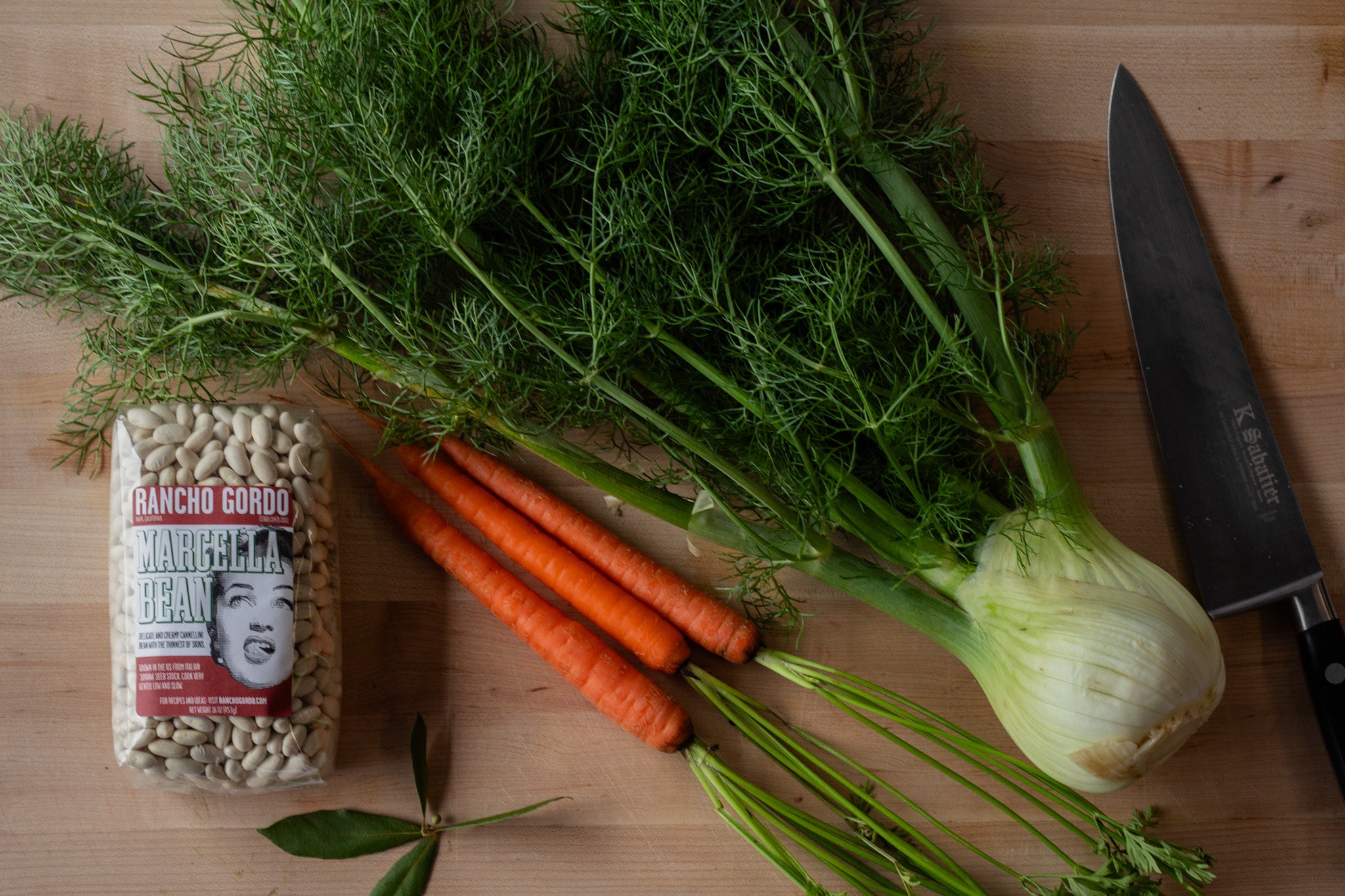A bag of Rancho Gordo Marcella beans with Fresh fennel and carrots on a cutting board 