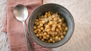A bowl of small garbanzos on a tablecloth with a spoon and red-striped napkin. 