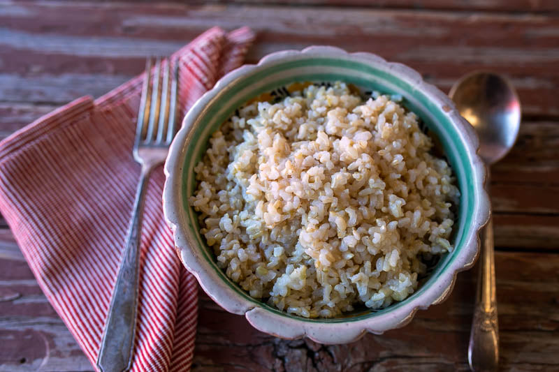 In a small bowl there's cooked California Brown Rice. In each side there's a silver fork and spoon.- Rancho Gordo