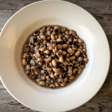 White bowl of cooked brothy Rancho Gordo Super Lucky Black Eyed Peas, on a wooden table