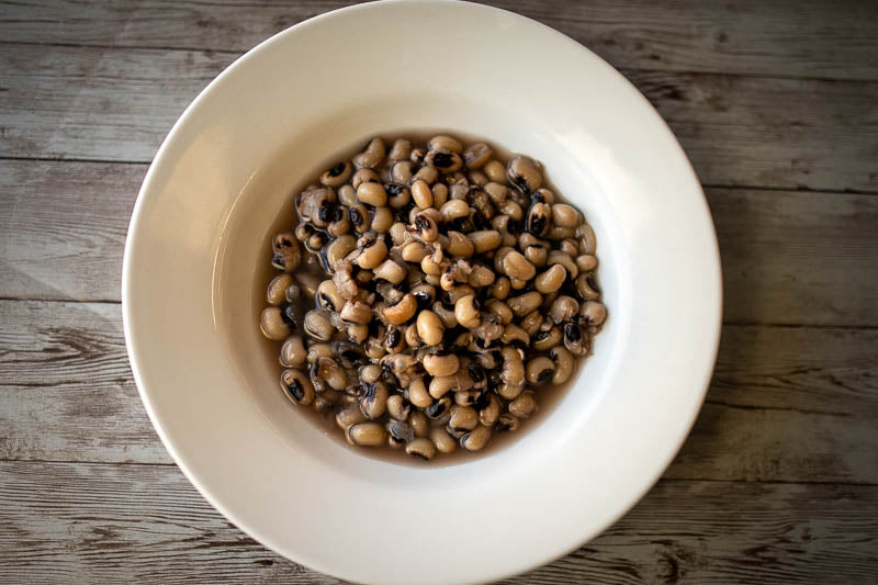 White bowl of cooked brothy Rancho Gordo Super Lucky Black Eyed Peas, on a wooden table