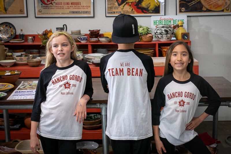 Three children wearing the Rancho Gordo Team Bean T-Shirt. one of them are showing the back of the shirt.