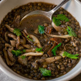 A mushroom dish with puglia lentils and flat lead parsley. The bowl rests on a wood table with a cloth napkin and a vintage spoon.