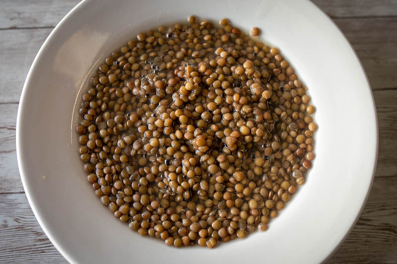 A white bowl of Puglia lentils rests on a wood table. 