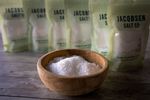 A bowl of Jacobsen Pure Flake Sea Salt with six bags in the background 