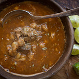 A bowl of pozole with limes in the background 