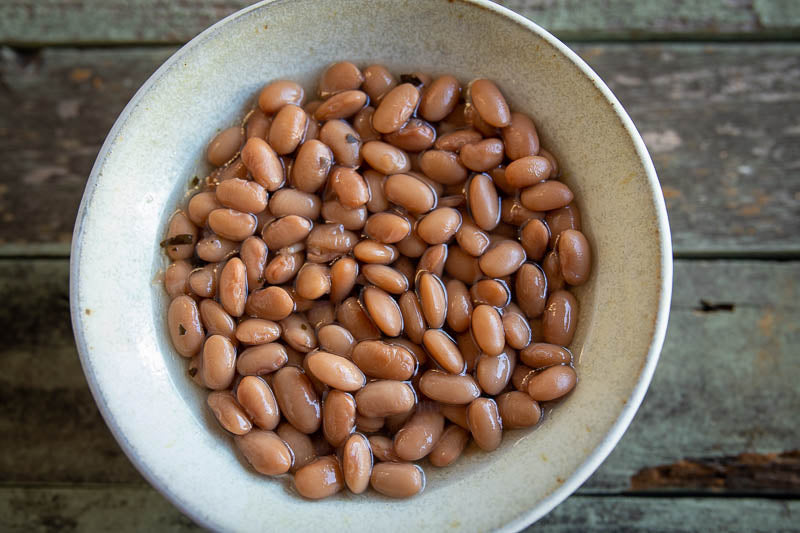A white bowl of cooked Mantequilla beans on a wooden table