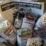 An Open box of the Bean Club with Marcella, Hidatsa Red, Cicerchia, French green lentils, Yellow Eye, Rio Zape, a jar of Oregano Indio, and recipes