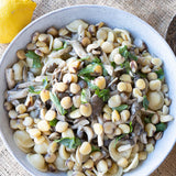 Cooked cicerchie beans mixed with sauteed mushrooms and pasta in a white serving bowl.