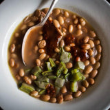 In a white bowl there's cooked Buckeye beans topped with nopal and salsa with a spoon 