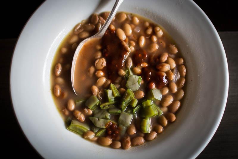 In a white bowl there's cooked Buckeye beans topped with nopal and salsa with a spoon 