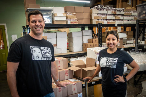 Rancho Gordo employee wearing Rancho Gordo Black T-Shirt. In the background there's beans and packages 